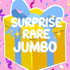 Peut inclure: Une boîte-cadeau jaune avec un ruban bleu et les mots "Surprise Rare Jumbo" dessus. La boîte est décorée d'étoiles dorées.