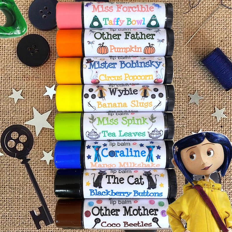 May include: Twelve lip balm tubes with colorful labels and names like Miss Forcible, Other Father, Mister Bobinsky, Wybie, Miss Spink, Coraline, The Cat, Other Mother. The labels have illustrations and text. The lip balms are arranged vertically in a row.