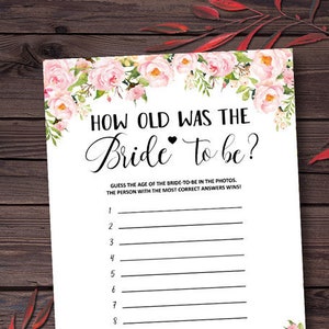 Puede incluir: Una tarjeta blanca de juego para la despedida de soltera con el texto "How Old Was The Bride to be?" en escritura negra. La tarjeta está decorada con acentos florales rosas y tiene líneas numeradas para adivinar las edades.