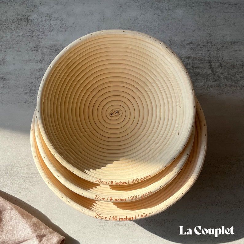 May include: Three round, light-colored proofing baskets of varying sizes, stacked on top of each other. The baskets have a spiral design and are labeled with measurements: 8 inches, 9 inches, and 10 inches. The brand name "La Couplet" is visible in the bottom right corner.