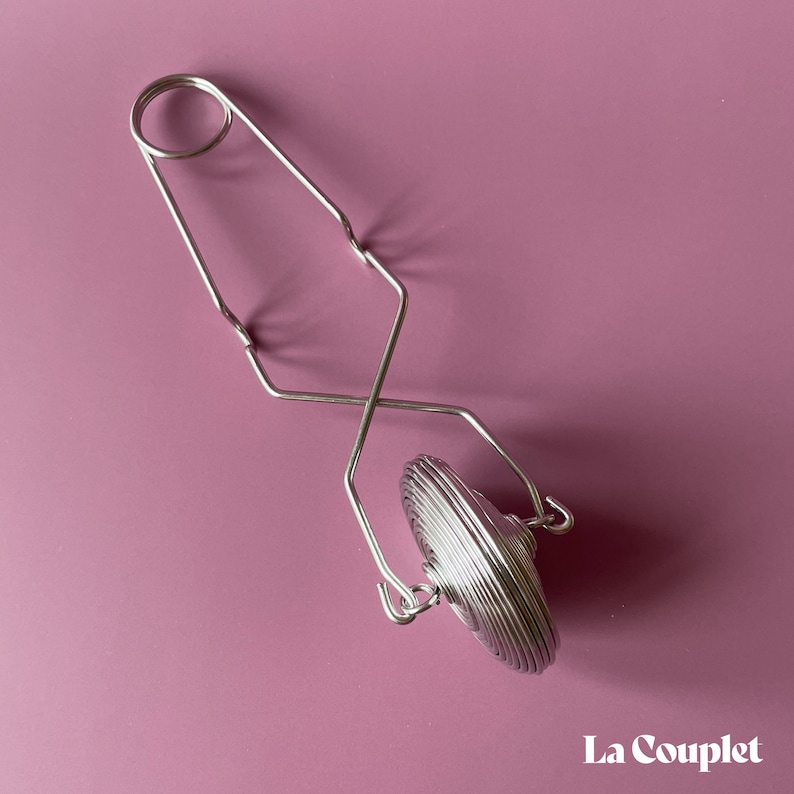 K&ouml;nnte beinhalten: Ein silberner Tee-Infuser mit einem federbelasteten Griff und einem runden, mehrschichtigen Netzfilter. Der Infuser ist f&uuml;r die Verwendung mit losen Tee-Bl&auml;ttern konzipiert.
