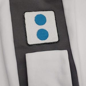 May include: White patch with a black border and two blue circles on a white background.