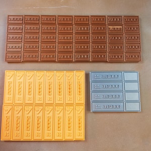 Op de afbeelding: Overzicht van rechthoekige blokken in bruin, geel en grijs. De bruine blokken zijn gemarkeerd met "1.000", de gele blokken hebben een symbool en tekst, en de grijze blokken zijn gemarkeerd met "10.000".