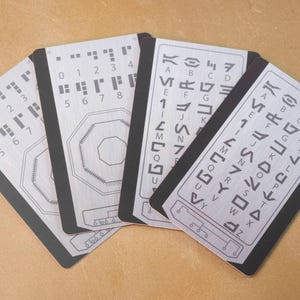 May include: Four black and silver cards with braille and alphabet symbols. The cards are arranged in a fan shape. The braille symbols are in rows of dots, and the alphabet symbols are in rows of lines.