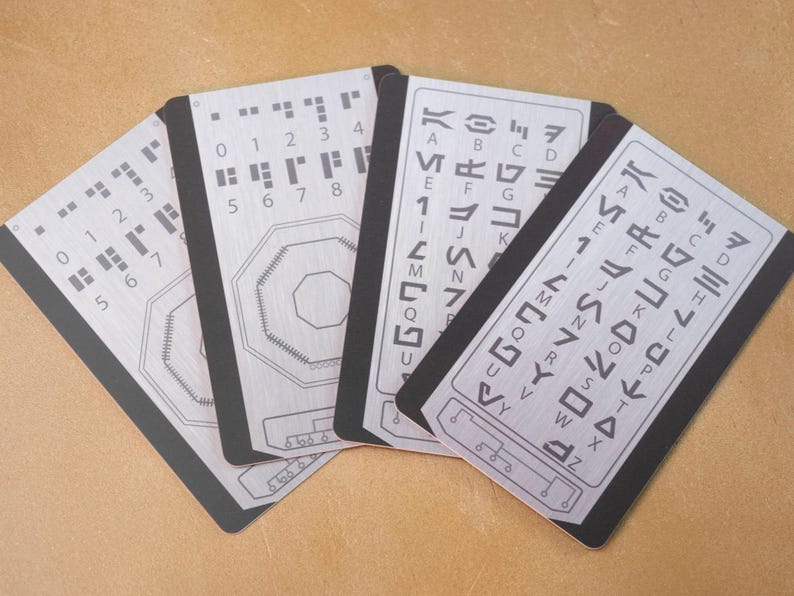May include: Four black and silver cards with braille and alphabet symbols. The cards are arranged in a fan shape. The braille symbols are in rows of dots, and the alphabet symbols are in rows of lines.