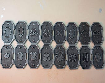 May include: Set of 16 silver metal tokens with various geometric designs. Each token has a raised design and a textured surface.