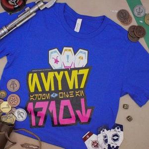 May include: A blue t-shirt with a graphic design featuring a yellow and pink logo with the text "1710", "ONE KI", "K7000", and "AMYUY7".