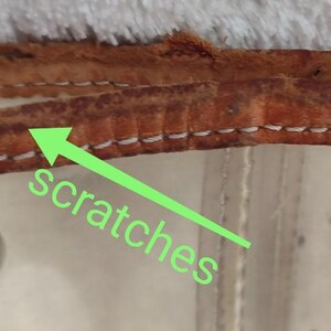 May include: Close-up of a brown leather strap with white stitching. The leather has scratches on the surface.