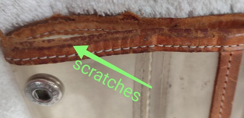 May include: Close-up of a brown leather strap with white stitching. The leather has scratches on the surface.