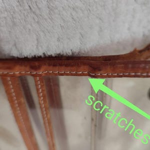 May include: Close-up of a clear plastic tote bag with brown leather trim. The leather trim has visible scratches.