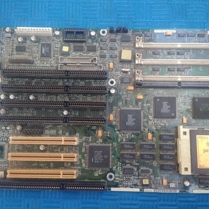 Op de afbeelding: Een vintage computer moederbord met diverse elektronische componenten, waaronder chips, slots en connectoren. Het bord is groen met gouden en zwarte accenten en heeft een Intel Pentium processor.