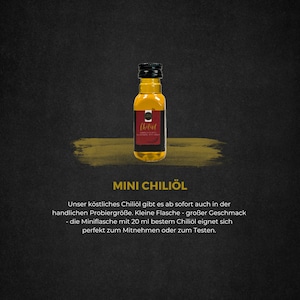 Könnte beinhalten: Eine kleine Flasche Chiliöl mit schwarzem Verschluss und einem rot-goldenen Etikett. Die Flasche ist mit einer goldgelben Flüssigkeit gefüllt. Unter der Flasche steht der Text "MINI CHILIÖL".