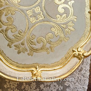 May include: A white and gold decorative tray with a scalloped edge and intricate gold leaf designs. The tray features a floral pattern with swirls and scrolls. The text "La Ballerina Gallery.com" is visible at the bottom of the tray.