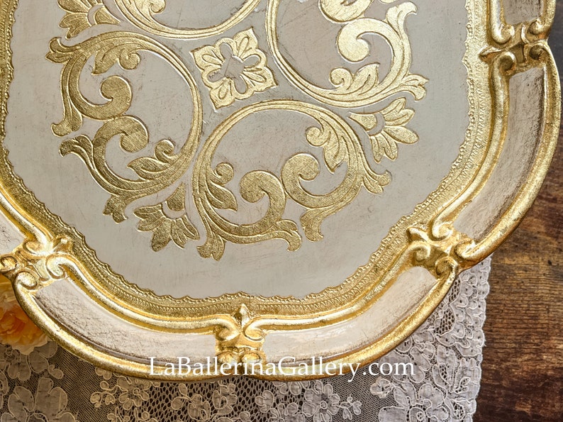 May include: A white and gold decorative tray with a scalloped edge and intricate gold leaf designs. The tray features a floral pattern with swirls and scrolls. The text "La Ballerina Gallery.com" is visible at the bottom of the tray.