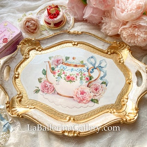 May include: A white and gold decorative serving tray with a painted design of a teapot and roses. The tray has two handles and a gold rim.