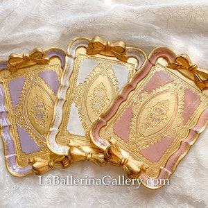 Puede incluir: Tres bandejas decorativas con ribetes dorados y diseños ornamentados. Las bandejas son en tonos lavanda, blanco y rosa.