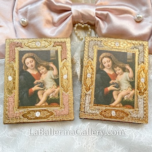 May include: Two ornate gold frames with pink accents, each containing a painting of the Madonna and Child. The frames are decorated with gold leaf and white pearl-like accents.