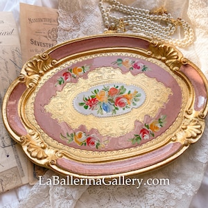 May include: An oval-shaped, pink and gold tray with a floral design. The tray has a raised rim and intricate details. The floral design features pink, yellow, and orange flowers.