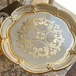 May include: A white and gold decorative tray with a scalloped edge and intricate gold leaf design. The tray is perfect for serving snacks or drinks.