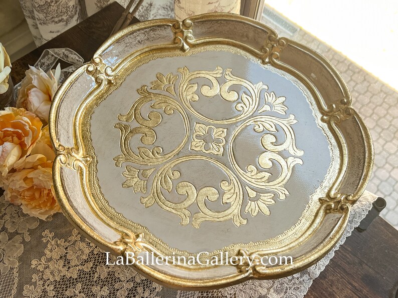 May include: A white and gold decorative tray with a scalloped edge and intricate gold leaf design. The tray is perfect for serving snacks or drinks.
