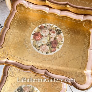 K&ouml;nnte beinhalten: Goldfarbene Dekotabletts mit floralem Mittelst&uuml;ck und gewelltem Rand. Die Tabletts haben einen rosa Rand und eine Blattgold-Oberfl&auml;che. Das florale Design zeigt Rosen in Rot-, Rosa- und Wei&szlig;t&ouml;nen. Die Website LaBallerinaGallery.com ist sichtbar.