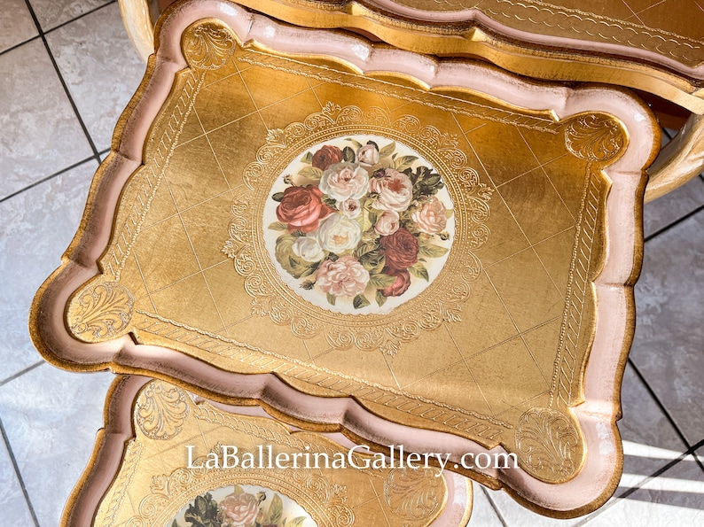 K&ouml;nnte beinhalten: Goldfarbene Dekotabletts mit floralem Mittelst&uuml;ck und gewelltem Rand. Die Tabletts haben einen rosa Rand und eine Blattgold-Oberfl&auml;che. Das florale Design zeigt Rosen in Rot-, Rosa- und Wei&szlig;t&ouml;nen. Die Website LaBallerinaGallery.com ist sichtbar.