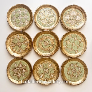 Puede incluir: Nueve platos decorativos con borde dorado y centro verde claro. Cada plato presenta un diseño en relieve único en oro y blanco. Los platos están dispuestos en una cuadrícula de 3x3. La dirección del sitio web LaBallerinaGallery.com es visible.