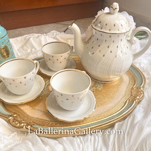 May include: A classic tea set featuring a white teapot, teacups, and saucers, embellished with gold detailing. The set is presented on a gold and blue decorative tray. The image conveys a sense of refined elegance and traditional charm.