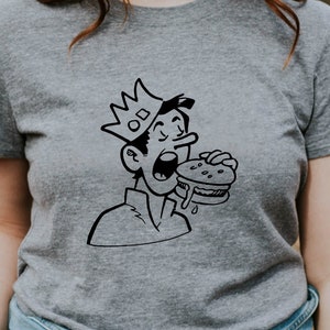 May include: A gray t-shirt with a black and white cartoon illustration of a person wearing a crown and eating a burger.