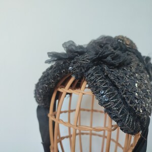 May include: A black sequined and lace headband with a bow on a brown wicker mannequin head.
