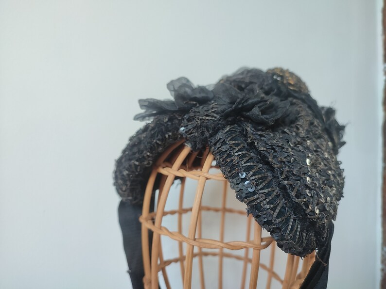 May include: A black sequined and lace headband with a bow on a brown wicker mannequin head.