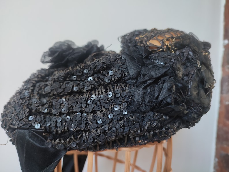 May include: A black hat with a large, ruffled bow and sequins. The hat is made of a soft, delicate fabric and has a vintage look.