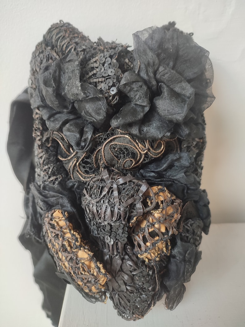 May include: A black vintage hat with intricate lace and sequin details. The hat features a large black flower made of fabric.