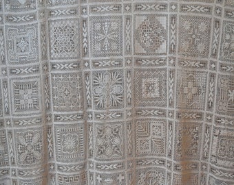 May include: A white lace tablecloth featuring a repeating pattern of intricate squares. The squares are composed of various designs, including floral motifs and geometric shapes.