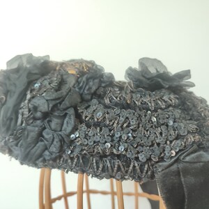 May include: A black hat with a large, ruffled bow and sequins. The hat is on a wooden hat stand.