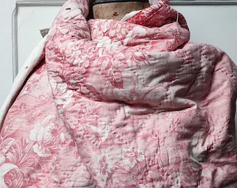 Puede incluir: Una colcha de color rosa con estampado floral drapeada sobre un maniquí de madera. La colcha está acolchada con un pequeño patrón de puntadas y tiene un aspecto descolorido y vintage.