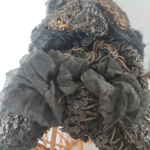May include: A black vintage hat with gold and black embroidery and sequins. The hat is on a wicker hat form.