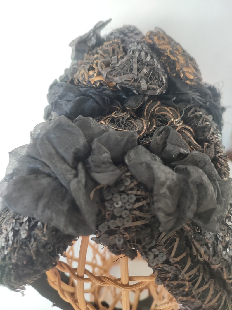 May include: A black vintage hat with gold and black embroidery and sequins. The hat is on a wicker hat form.