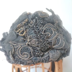 May include: A black vintage hat with intricate lace detailing and black beads. The hat is adorned with gold embroidery and has a slightly ruffled texture.