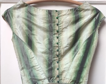 May include: A vintage-style, green and gray striped top with a scoop neckline and cap sleeves. The top features a series of green buttons down the back and is made of a silky, possibly satin, material. The garment is displayed on a wooden hanger.