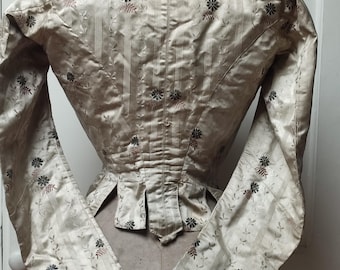 Puede incluir: Chaqueta vintage color crema con mangas largas. La chaqueta presenta un estampado floral con rayas verticales y se exhibe en un maniquí. Las mangas son largas y ajustadas, y la chaqueta tiene una cintura entallada.
