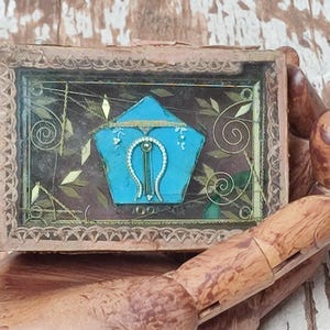Peut inclure: Une petite boîte en bois avec un dessus en verre, contenant un objet décoratif bleu et or. La boîte a un motif sculpté autour du bord et le verre est fissuré à certains endroits.
