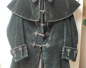 Könnte beinhalten: Eine dunkelgrüne Samtjacke mit einem großen Kragen und dekorativen Verzierungen. Die Jacke hat einen langen, fließenden Stil und verfügt über eine Reihe von Knöpfen an der Vorderseite.