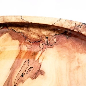 May include: A wooden bowl with a natural wood finish. The bowl has a unique grain pattern with brown and pink hues. The bowl is made of wood and has a smooth, polished surface.