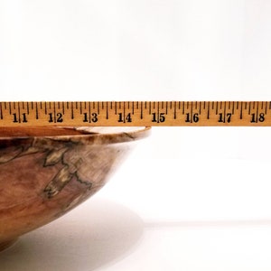 May include: A wooden bowl with a natural wood grain pattern. The bowl is 15 inches wide and has a light brown color.