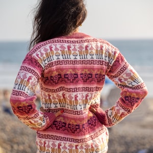 May include: A woman wearing a pink and white sweater with a geometric pattern. The sweater features a repeating design of llamas and other geometric shapes.