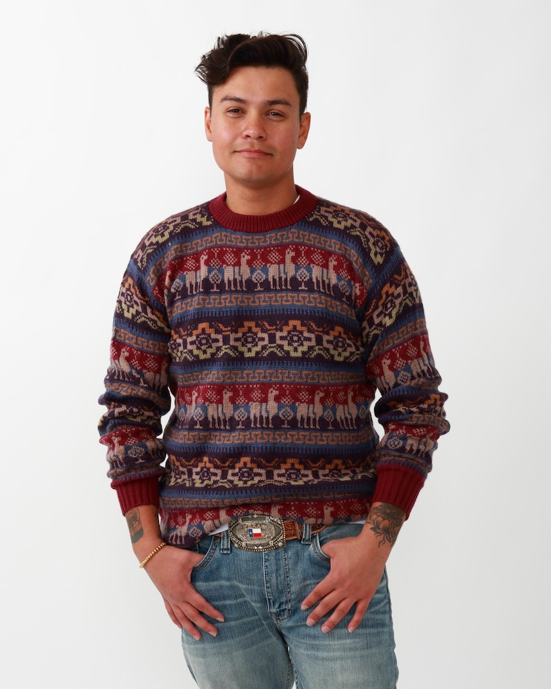 May include: A burgundy, blue, and beige patterned sweater with a crew neck and long sleeves. The sweater features a geometric design with llamas.