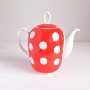 May include: A red ceramic teapot with white polka dots. The teapot has a white handle, spout, and lid with a loop. The design is a classic and cheerful style, perfect for serving tea.