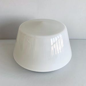 May include: A white, glossy ceramic bowl with a rounded base and a slightly flared rim. The bowl has a smooth, reflective surface. The bowl is sitting on a white surface. The interior is not visible.