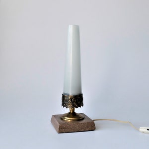 May include: A vintage table lamp with a white, conical shade. The lamp features a brass base with decorative detailing and a rectangular, speckled stone base. The lamp is connected to a power cord with an on/off switch.
